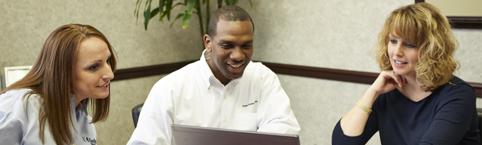 three smiling employees consulting at a computer